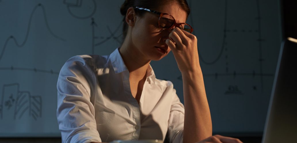 Mulher trabalhando à noite estressada, ilustrando um ambiente corporativo com clima organizacional tóxico.